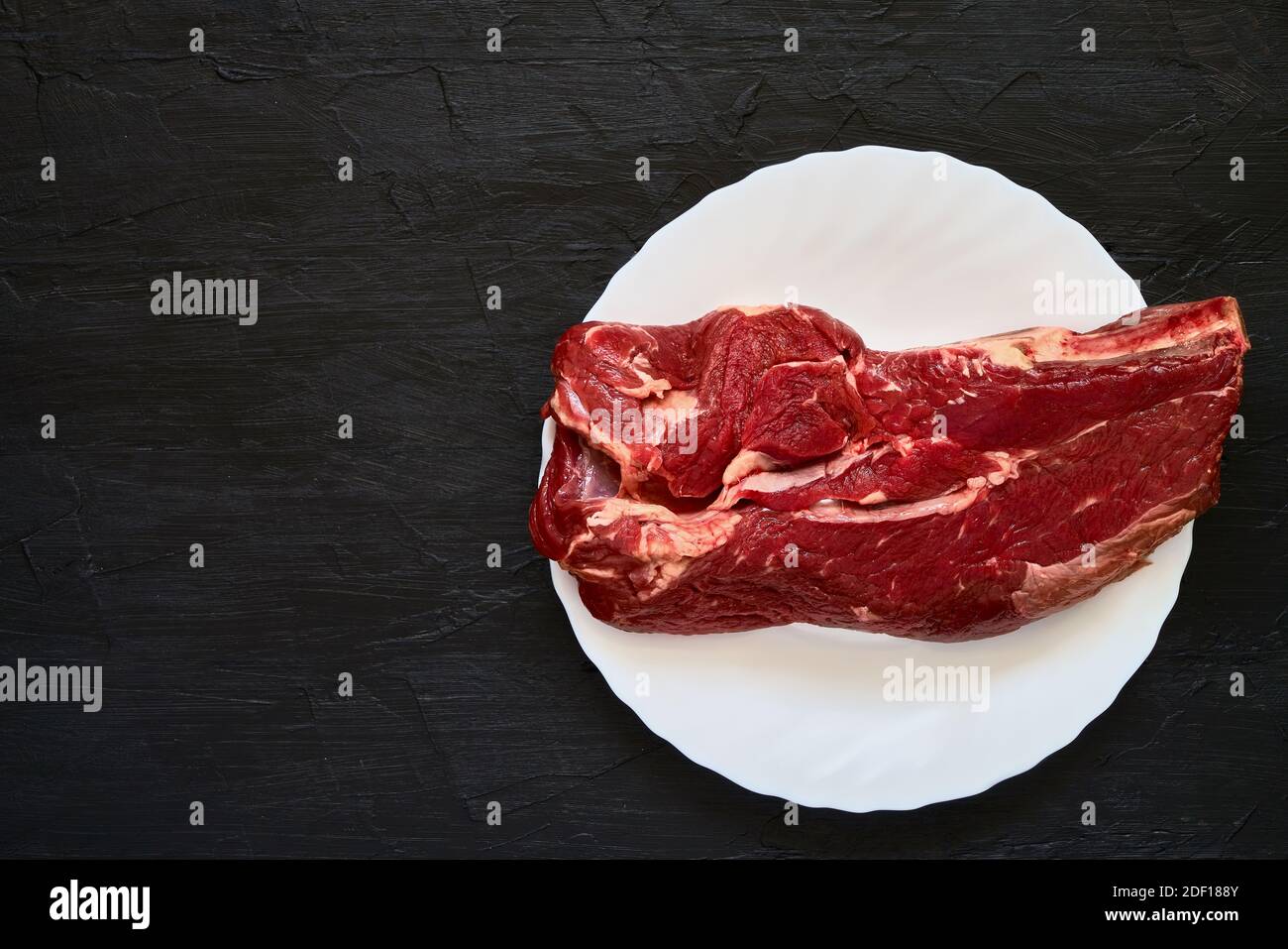 Viande de bœuf fraîche sur plaque blanche sur fond noir. Espace de copie, vue de dessus. Aliments biologiques Banque D'Images