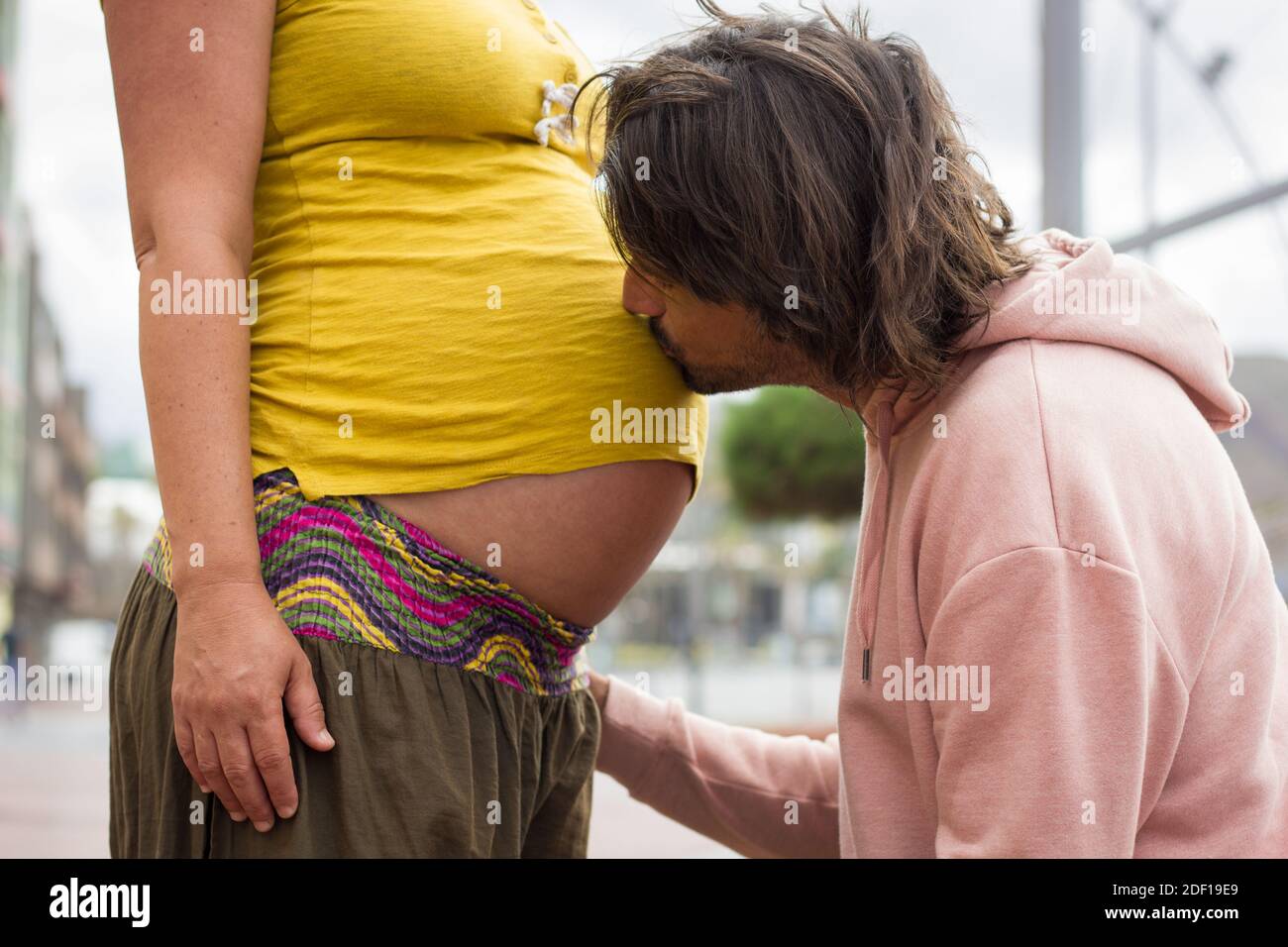 Un jeune papa aux cheveux longs embrasse le grand ventre de sa mère sur une chemise jaune. Un couple enthousiaste attend bébé. Amour affection, nouvelle vie, concept de parentalité Banque D'Images