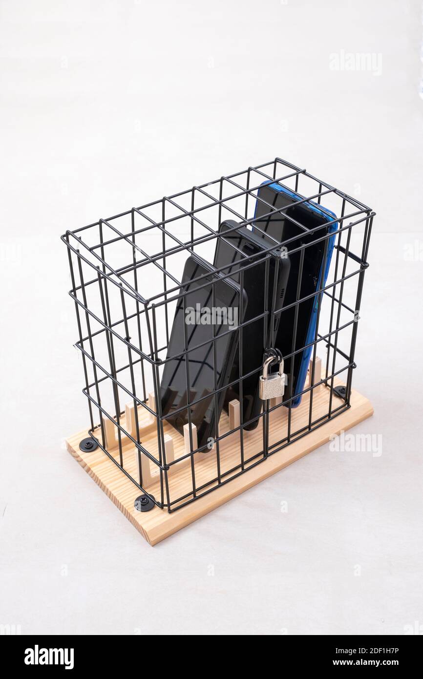 trois téléphones mobiles enfermés dans une cage avec un cadenas, concept d'isolement social ou d'abus de téléphone et de réseaux sociaux, fond blanc, vertical Banque D'Images