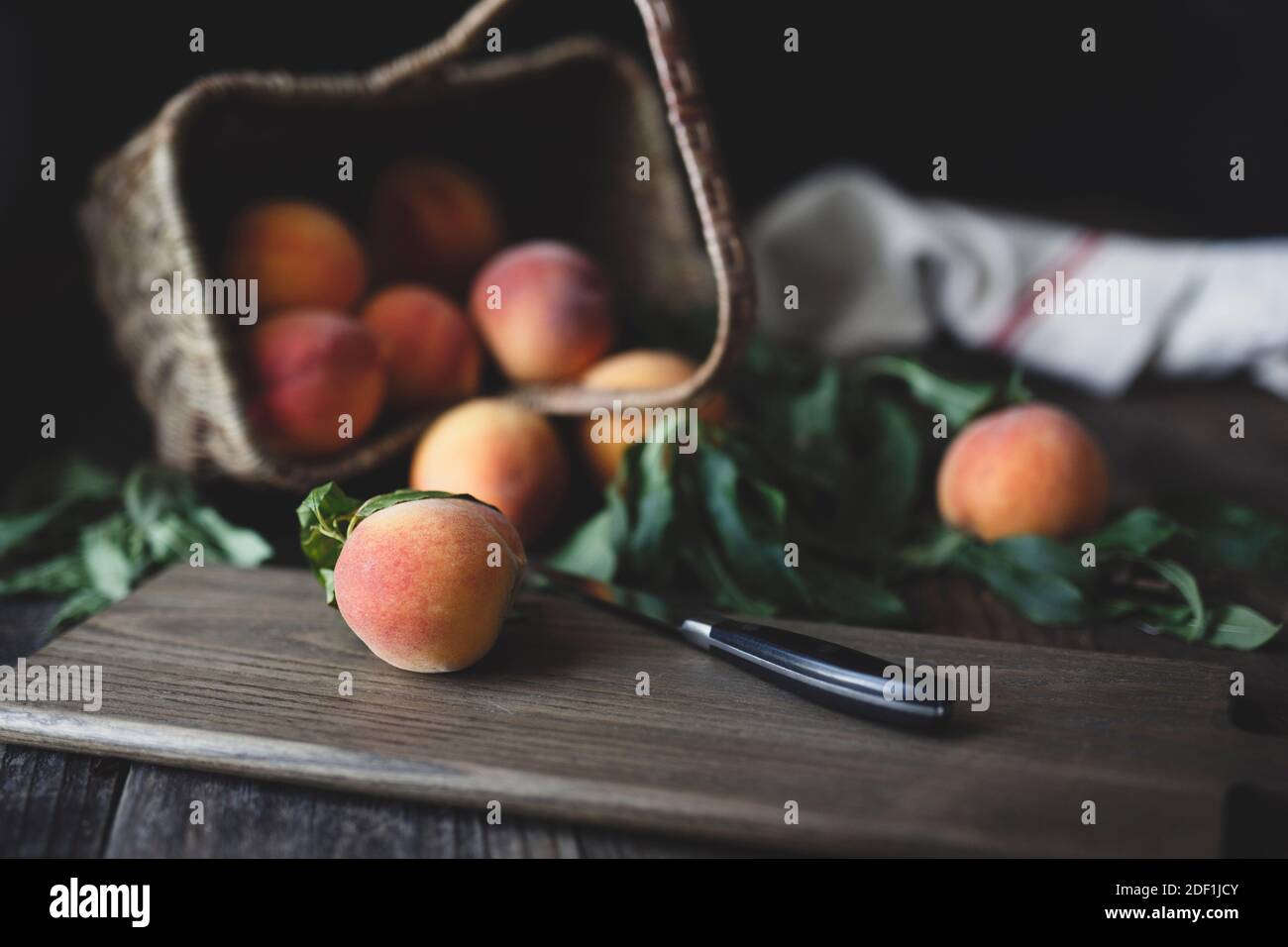 pêches fraîches dans le panier à pointes et sur la planche à découper avec couteau Banque D'Images