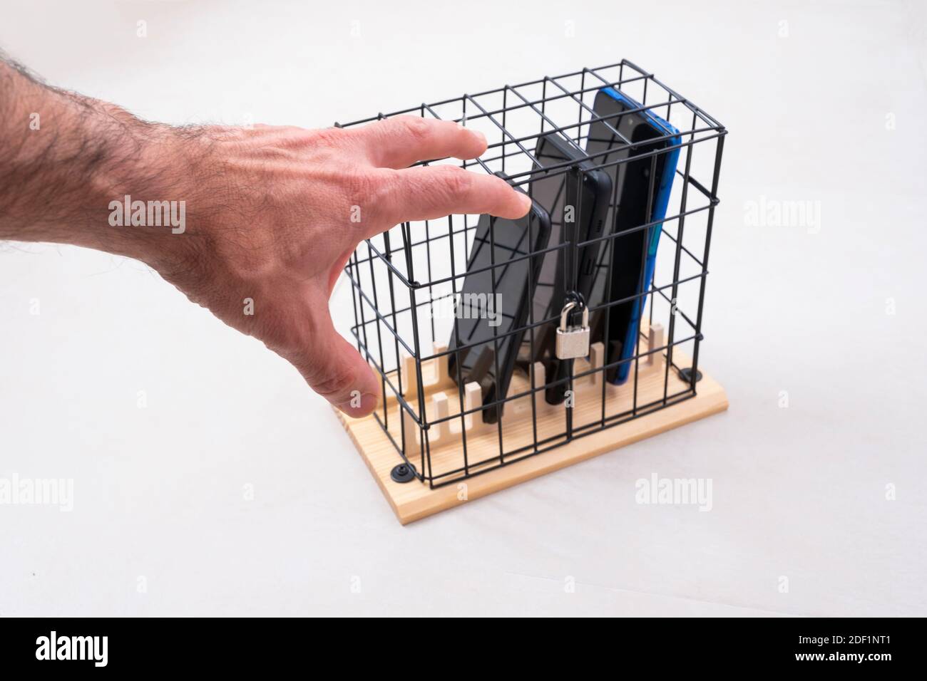 main essayant d'attraper trois téléphones mobiles enfermés dans une cage avec un cadenas, concept d'isolement social ou d'abus de téléphone et les réseaux sociaux, blanc backgr Banque D'Images