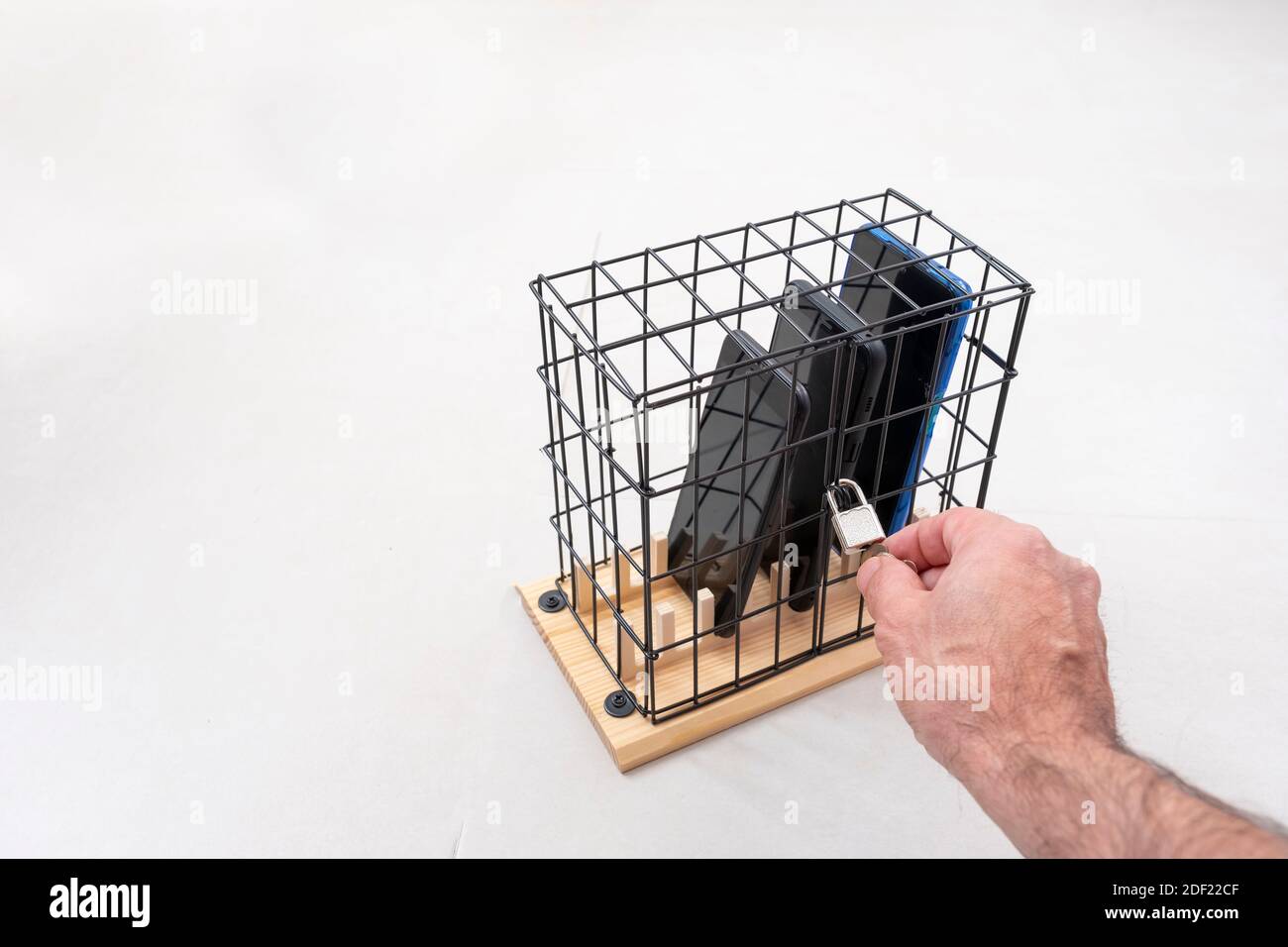 main ouvrant ou fermant la serrure sur une cage avec trois téléphones mobiles verrouillés dans une cage avec un cadenas, concept d'isolement social ou d'abus de téléphone et ainsi de suite Banque D'Images