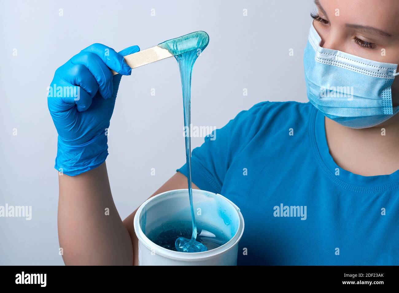 Un maître sugaring en gants bleus et un masque médical tient un bâton de cire de sucre bleu. Épilation et concept de beauté Banque D'Images