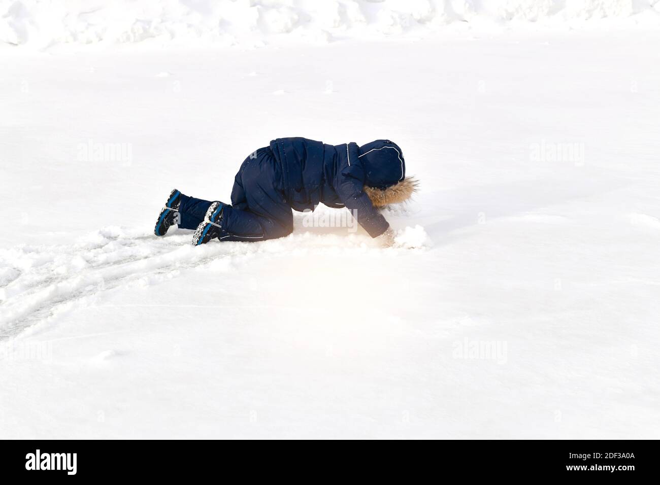 Un enfant s'élanche sur tous les fours dans la neige dans une combinaison d'hiver avec une capuche en fourrure. Laissant un sentier derrière lui. Banque D'Images