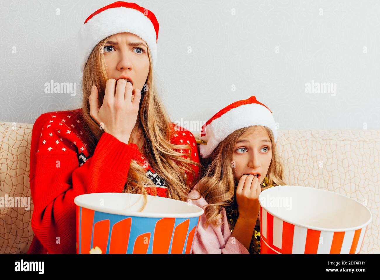 La mère et sa petite fille, vêtues de chapeaux du Père Noël, regardent des films et mangent du pop-corn, assis sur le canapé. Concept de Noël Banque D'Images