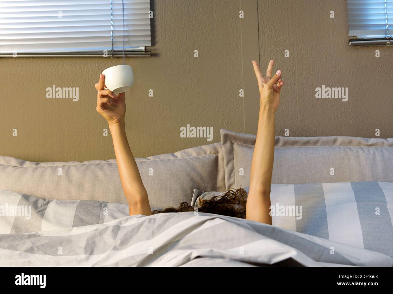 Femme incognito tenant une tasse de café, s'étirant dans le lit, montrant les mains sous la couverture. Concept Happy Morning Banque D'Images