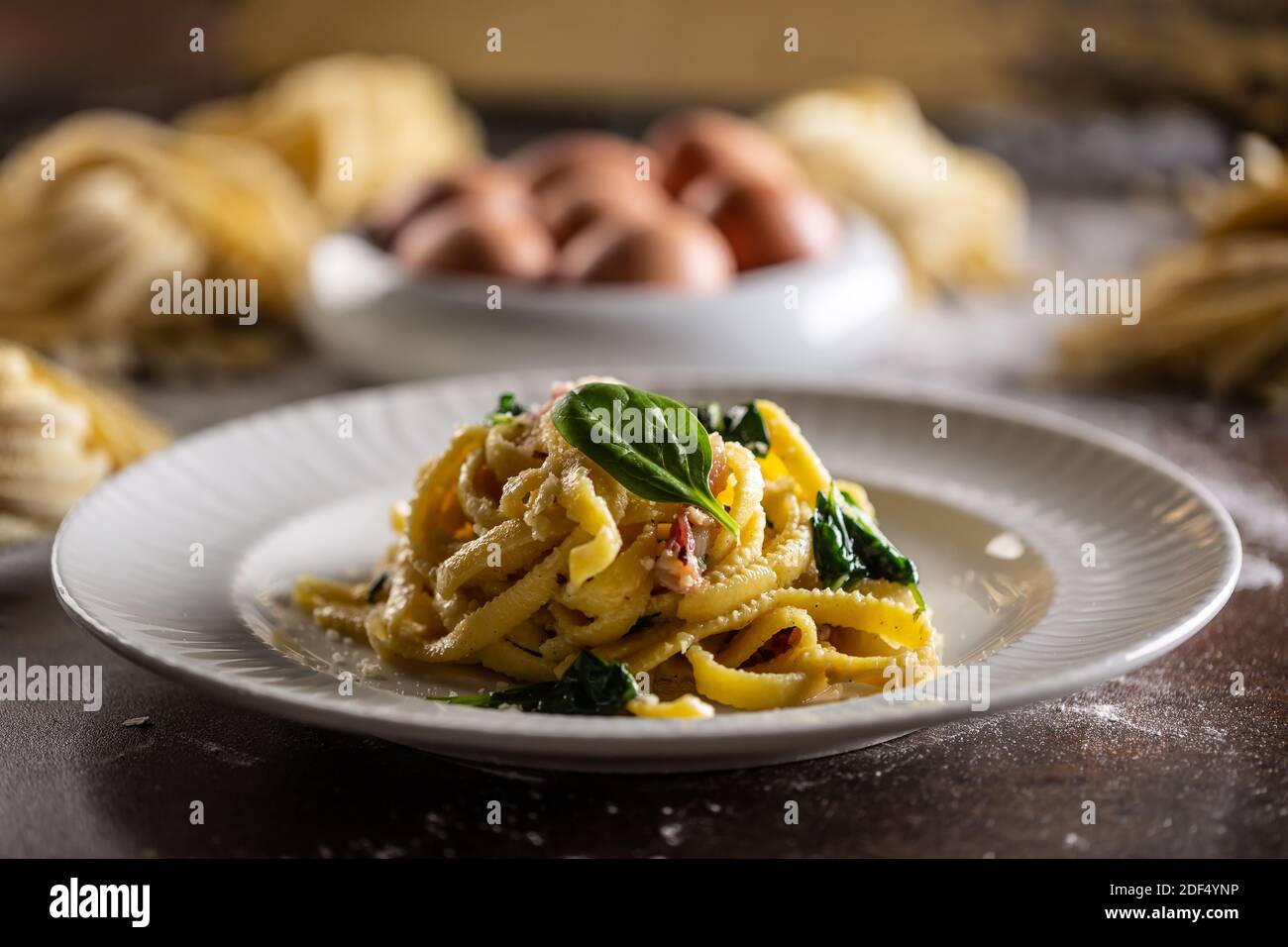 Pâtes fraîches cuites à la fettuccine servies sur une assiette avec des épinards et du bacon. Banque D'Images