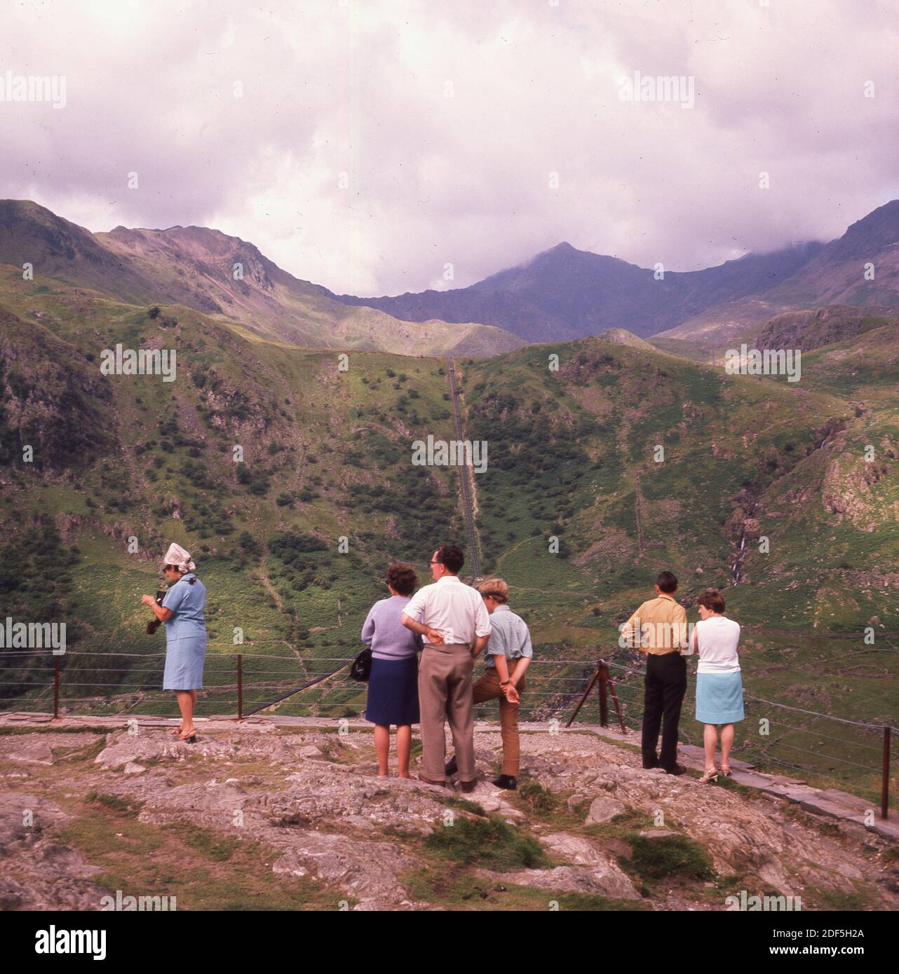 Années 1960, historique, printemps et visiteurs haut sur un point de vue sur le mont Snowdon, au pays de Galles, surplombant la chaîne de montagnes dans le parc national. À cette époque, les gens allaient dans de tels endroits dans des vêtements de tous les jours normaux, pas dans des vêtements synthétiques et des bottes de montagne! Banque D'Images