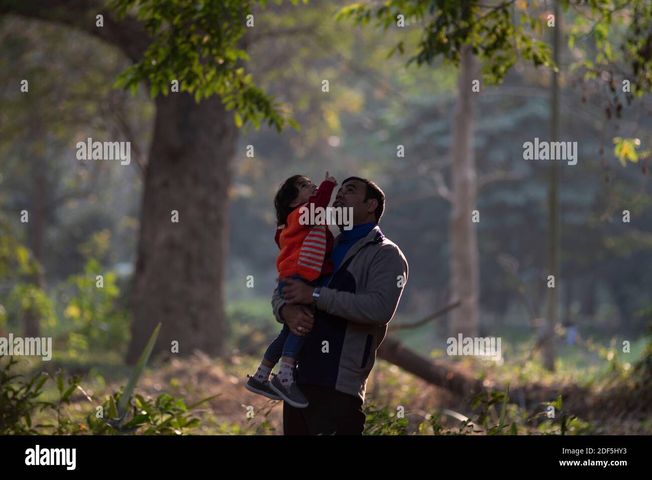 Un père de brunette indien et son bébé garçon en vêtements d'hiver s'appréciant dans l'après-midi d'hiver sur un champ d'herbe sec en arrière-plan de forêt. Banque D'Images