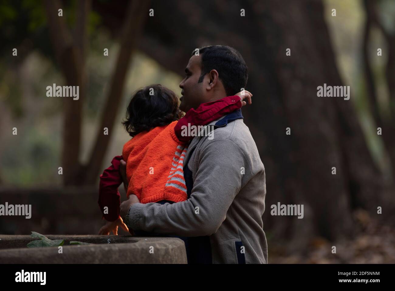 Un père de brunette indien et son bébé garçon en vêtements d'hiver s'appréciant dans l'après-midi d'hiver sur un champ d'herbe sec en arrière-plan de forêt. Banque D'Images