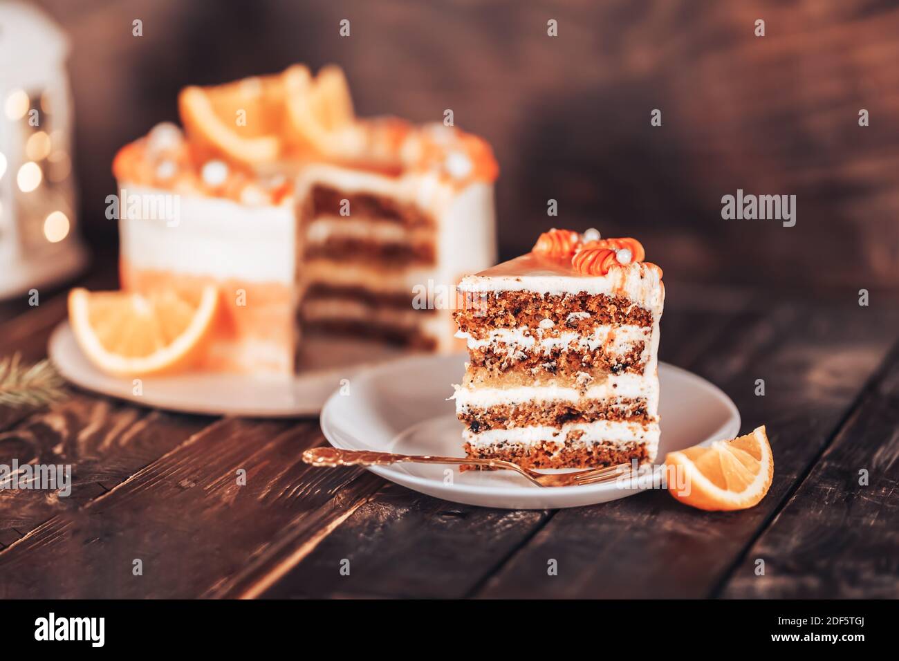 Découper le gâteau sur une assiette blanche avec une fourchette. Des bonbons pour toutes les vacances. Sur un fond de bois avec des guirlandes et une lanterne. Morceau de gâteau sur une assiette blanche Banque D'Images