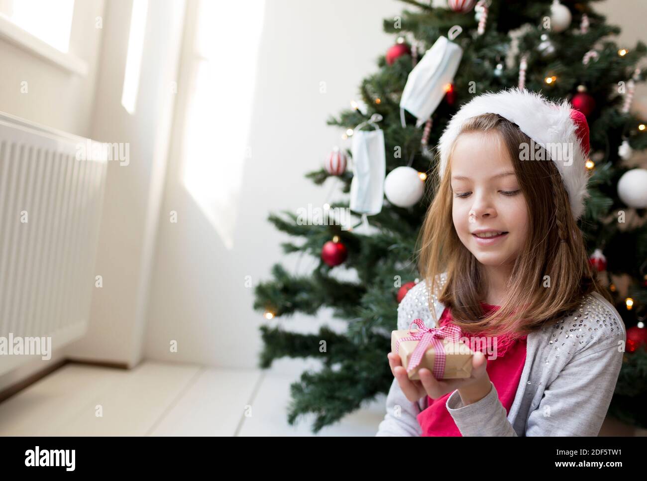 Jeune fille dans la clause de santa chapeau avec des cadeaux de Noël dans Devant un arbre de Noël avec des masques Banque D'Images