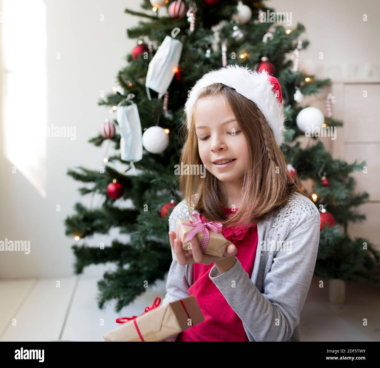 Jeune fille dans la clause de santa chapeau avec des cadeaux de Noël dans Devant un arbre de Noël avec des masques Banque D'Images