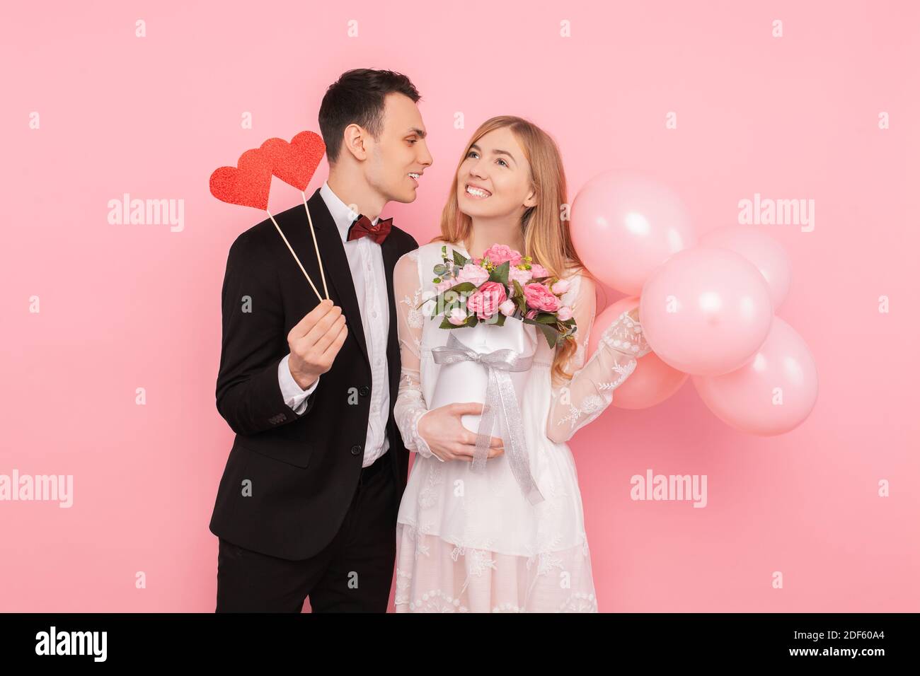 Un couple aimant, un homme tient deux coeurs en papier, et une femme tient un bouquet de fleurs et de ballons Banque D'Images