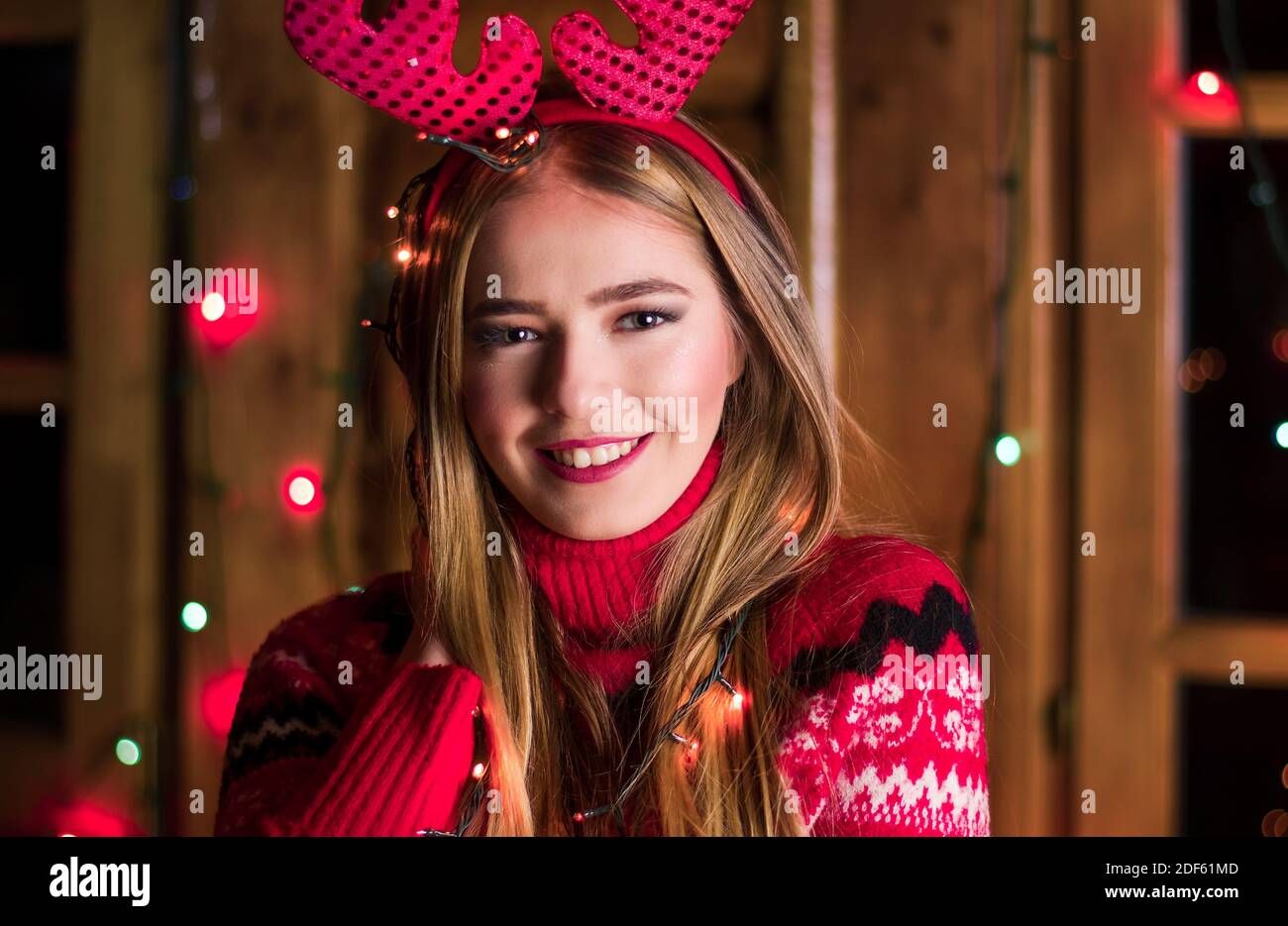 Belle fille avec lumières de fête wearing red sweater dans une maison en bois rond Banque D'Images
