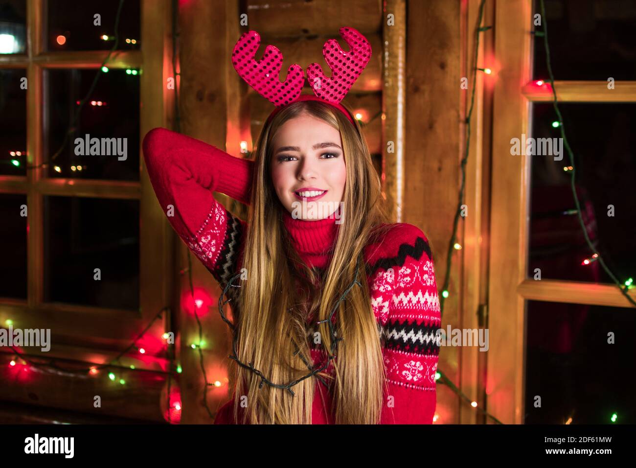 Belle fille avec lumières de fête wearing red sweater dans une maison en bois rond Banque D'Images