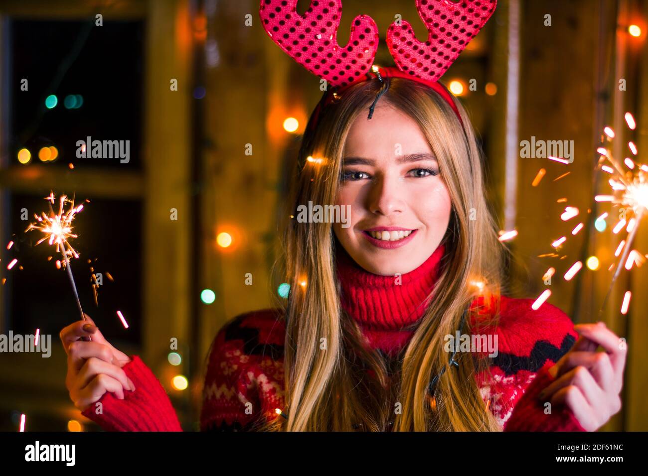 Jeune femme tirant des étincelles de fête tout en célébrant Noël vêtue de  rouge pull dans une cabine en bois Photo Stock - Alamy