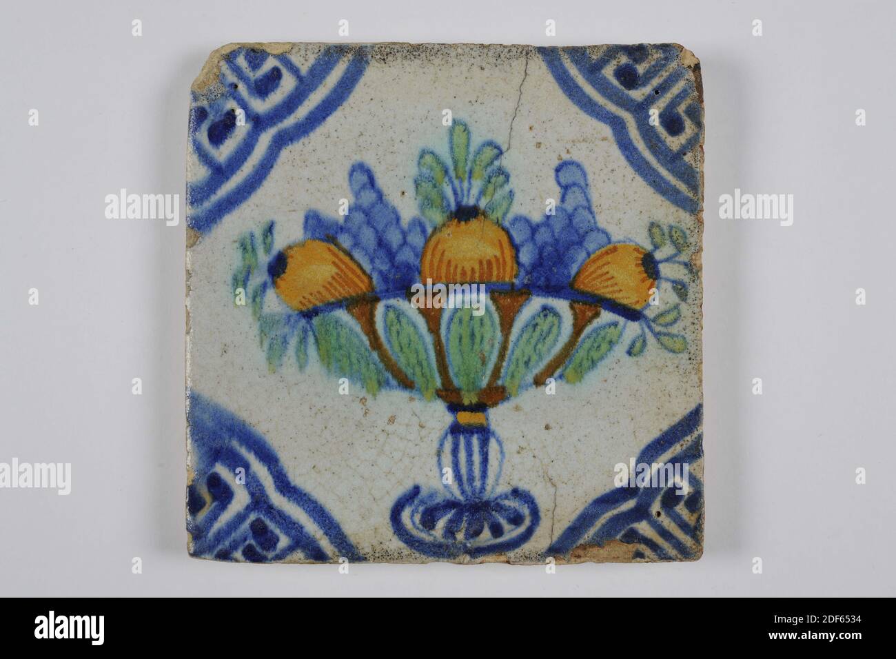 Carreau de mur, Anonyme, première moitié du XVIIe siècle, glaçure d'étain, faïence, général: 13 x 13 x 1,3cm (130 x 130 x 13mm), bouquet de raisins, bol de fruits, fruit, pays-Bas du Nord, tuile murale de faïence recouverte de glaçure d'étain. Multicolore peint en bleu, vert, orange et orange-brun, avec un dessin bleu. La tuile représente un bol de fruits avec des grappes de raisins et des fruits orange. Le carrelage est orné d'un motif de coin. Avec sur le dos la peinture du monogramme IVS en bleu, 1985 Banque D'Images