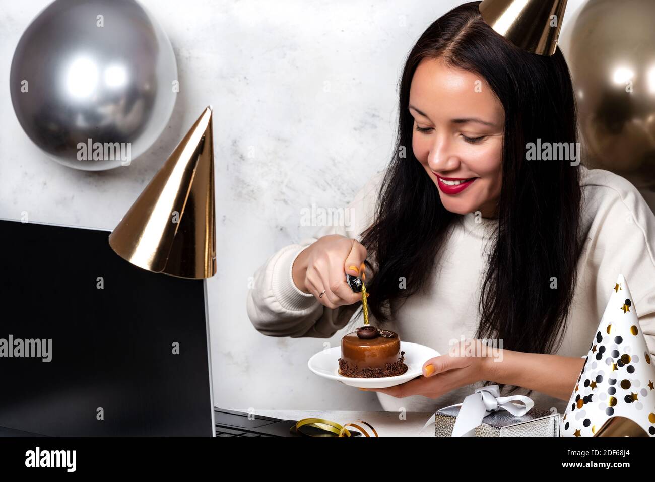 Une femme allume une bougie sur un gâteau de fête et fait une vidéo L'appel célèbre l'anniversaire en ligne pendant la quarantaine en raison de la pandémie COVID-19 Banque D'Images