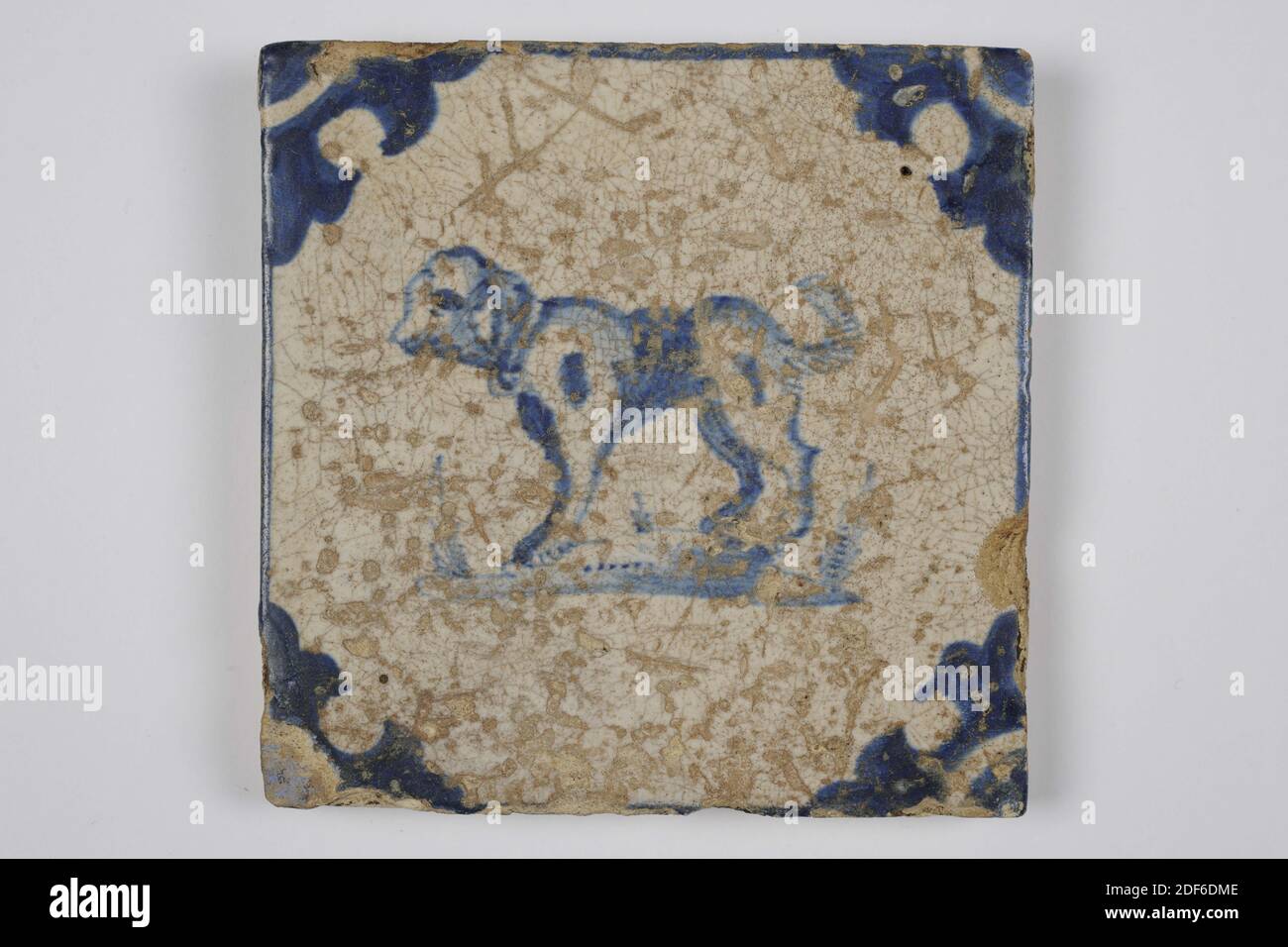 Carreau de mur, Anonyme, entre 1640-1700, glaçure d'étain, faïence, général: 13.2 x 13.2 x 1.1cm (132 x 132 x 11mm), chien, carreau de mur en faïence recouvert de glaçure d'étain et peint en bleu. La mosaïque représente un chien orienté vers la droite au centre. L'animal a les pattes avant du sol et un objet dans la bouche. La tuile a une tête de boeuf comme un motif de coin, 1995 Banque D'Images