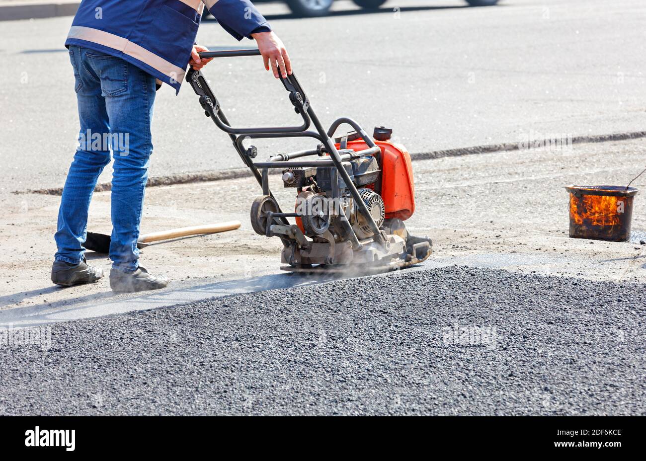 Un agent de service routier comboîte l'asphalte sur une section de route clôturée avec un compacteur à plaque vibrante à essence. Banque D'Images