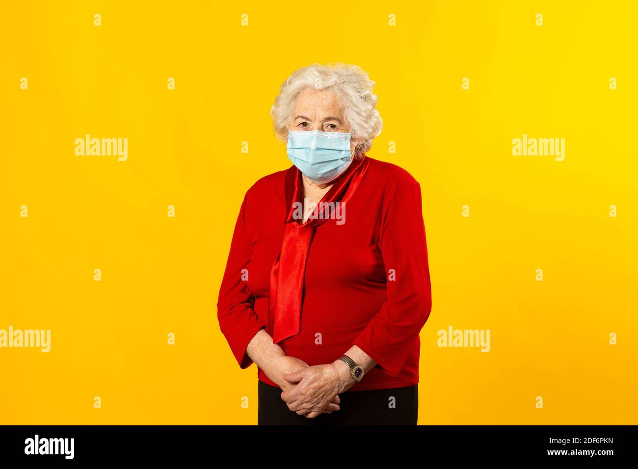 Portrait en studio d'une femme âgée portant une chemise rouge et un masque chirurgical, sur fond jaune Banque D'Images