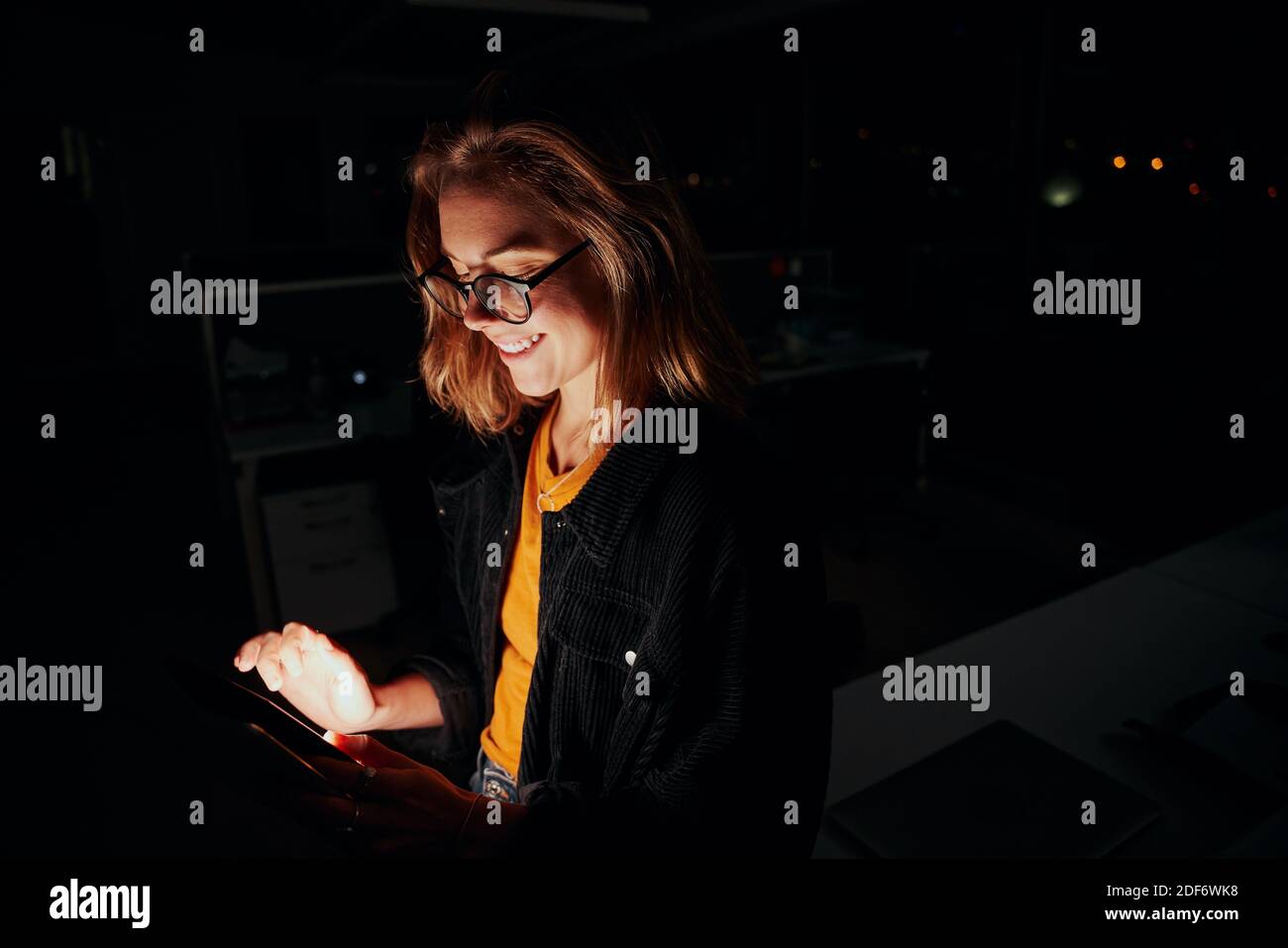 Portrait d'une femme cadre heureuse debout près du bureau utilisation d'une tablette numérique dans une salle de bureau sombre Banque D'Images
