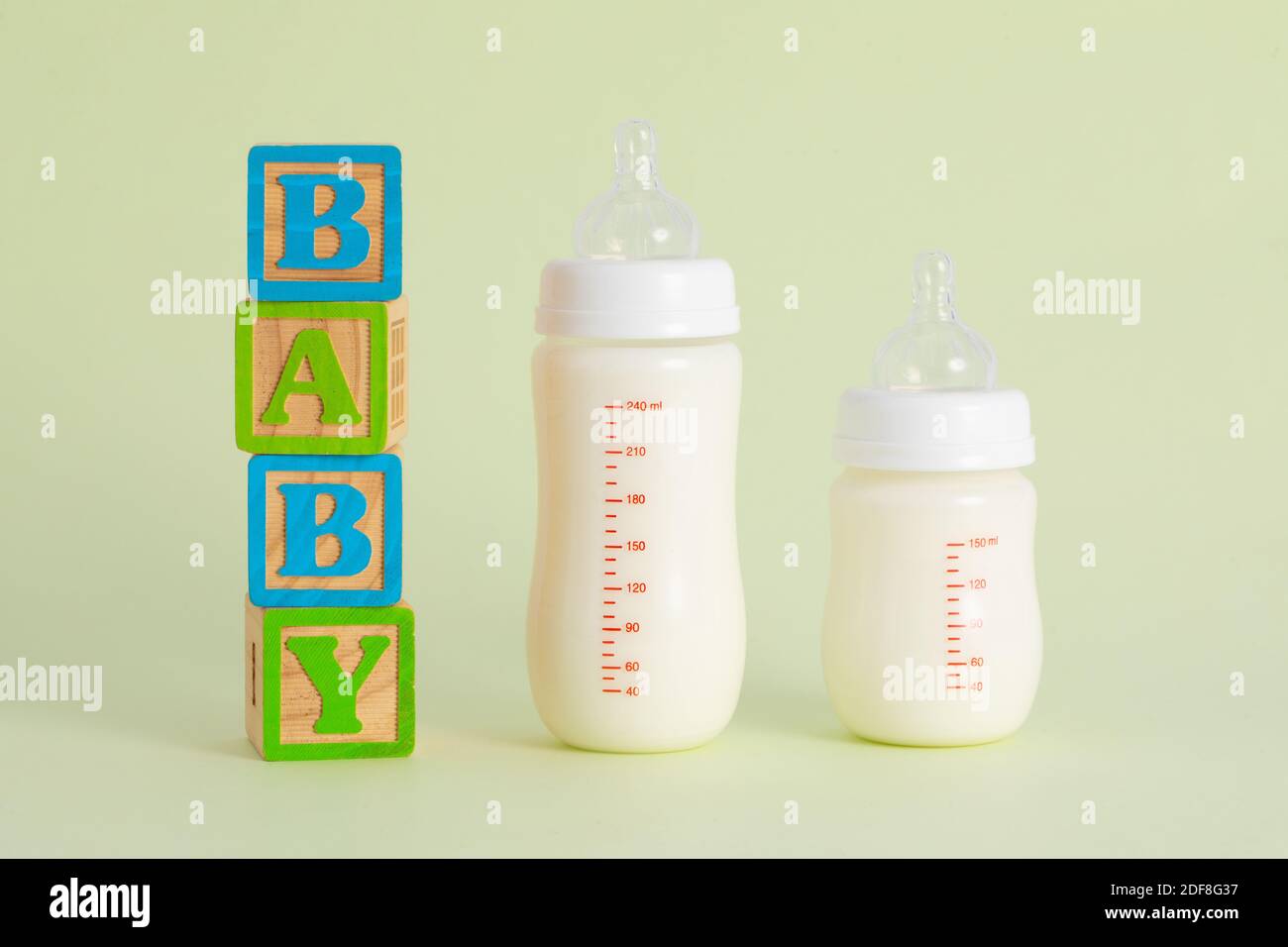 Un « Baby » écrit en bois à côté de bouteilles pleines de lait sur fond vert pastel Banque D'Images
