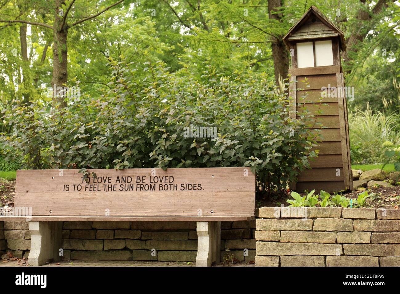 Un Banc De Parc En Bois Grave Avec Une Citation Inspirante Le Long D Un Mur De Soutenement De Pierre Arbustes Arbres Et Une Maison De Feu De Bois A Janesville Wisconsin Etats Unis