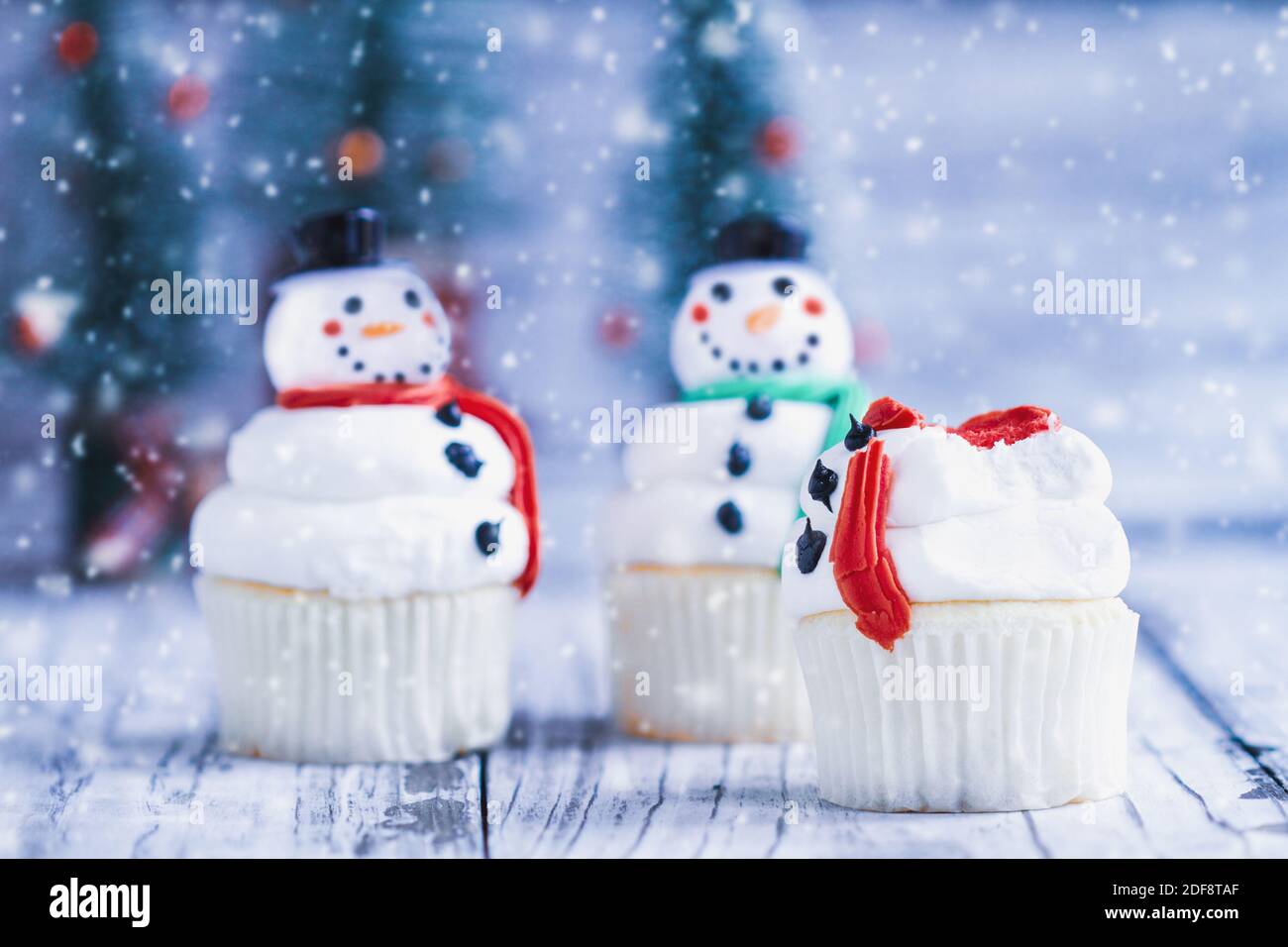 Gâteau de Noël glacé bonhomme de neige avec une partie mordue ou mangé. Autres bonshommes de neige avec nez de carotte, chapeau de père Noël et foulard. Mise au point sélective arrière-plan flou. Banque D'Images