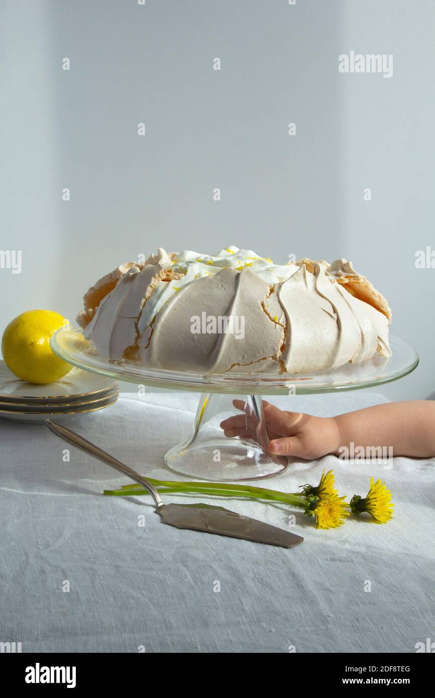 La Main De L Enfant Atteint Pour Le Gateau Meringue Pavlova Avec Fouette Creme Et Citron Sur Support A Gateau En Verre Photo Stock Alamy