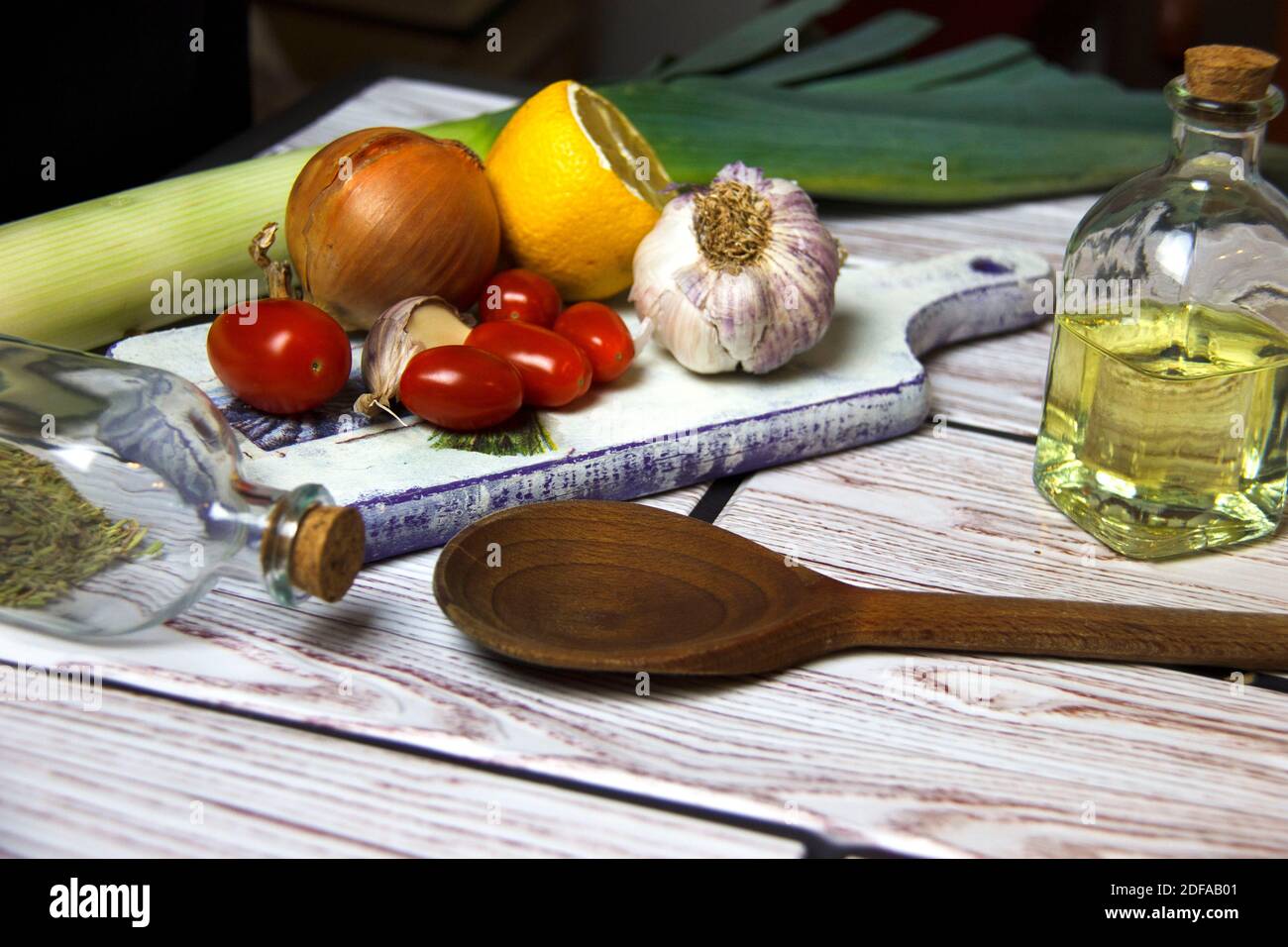 Fond de cuisson. Huile dans une bouteille, ail, oignon, tomates et citron sur une planche à découper. Préparation des aliments. Concept de saine alimentation. Banque D'Images