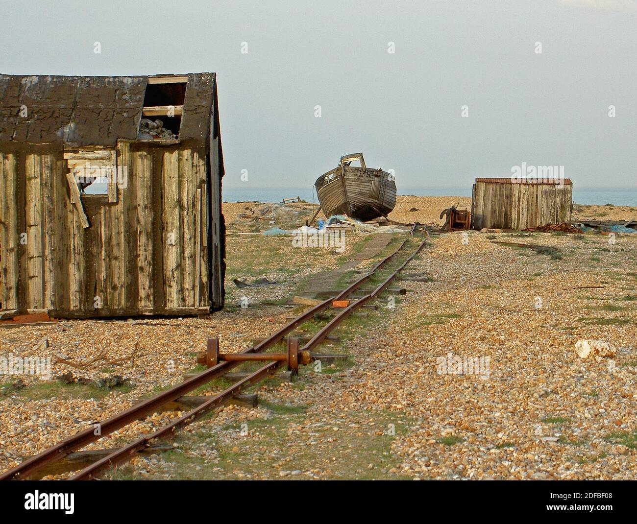 Une ancienne voie ferrée désaffectée, utilisée pour amener le rattrapage des pêcheurs au-dessus de la plage de galets, passe des cabanes abandonnées et la coque d'un vieux bateau de pêche. Banque D'Images