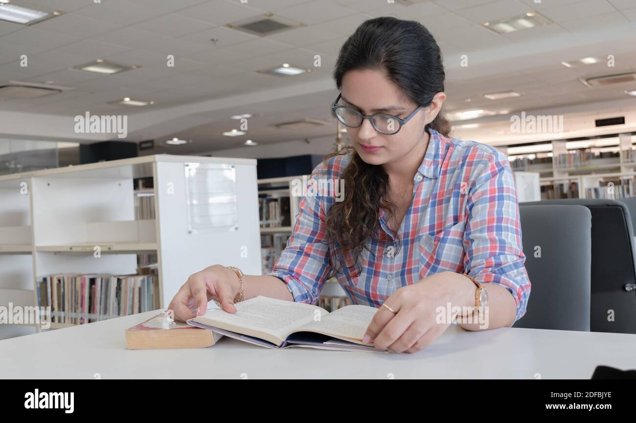 Belle et intelligente jeune fille avec des lunettes étudiant dur dans la bibliothèque publique pour les examens à venir. Tous les étudiants de l'université peuvent connecter cela. Banque D'Images