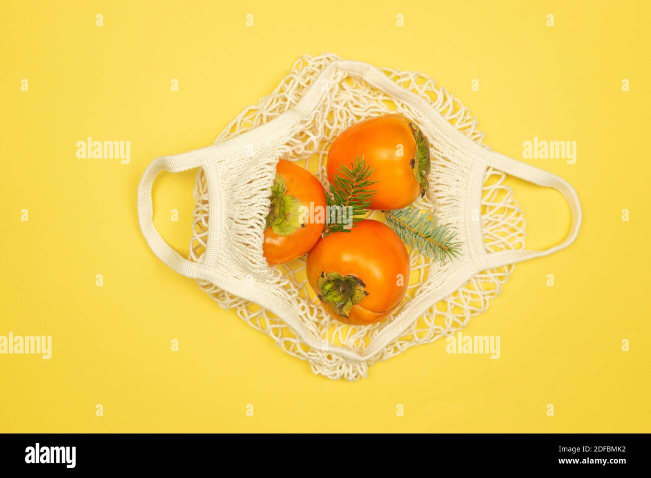 Les fruits persimmon se trouvent dans le sac de filet blanc sur fond jaune. Concept d'alimentation saine Banque D'Images