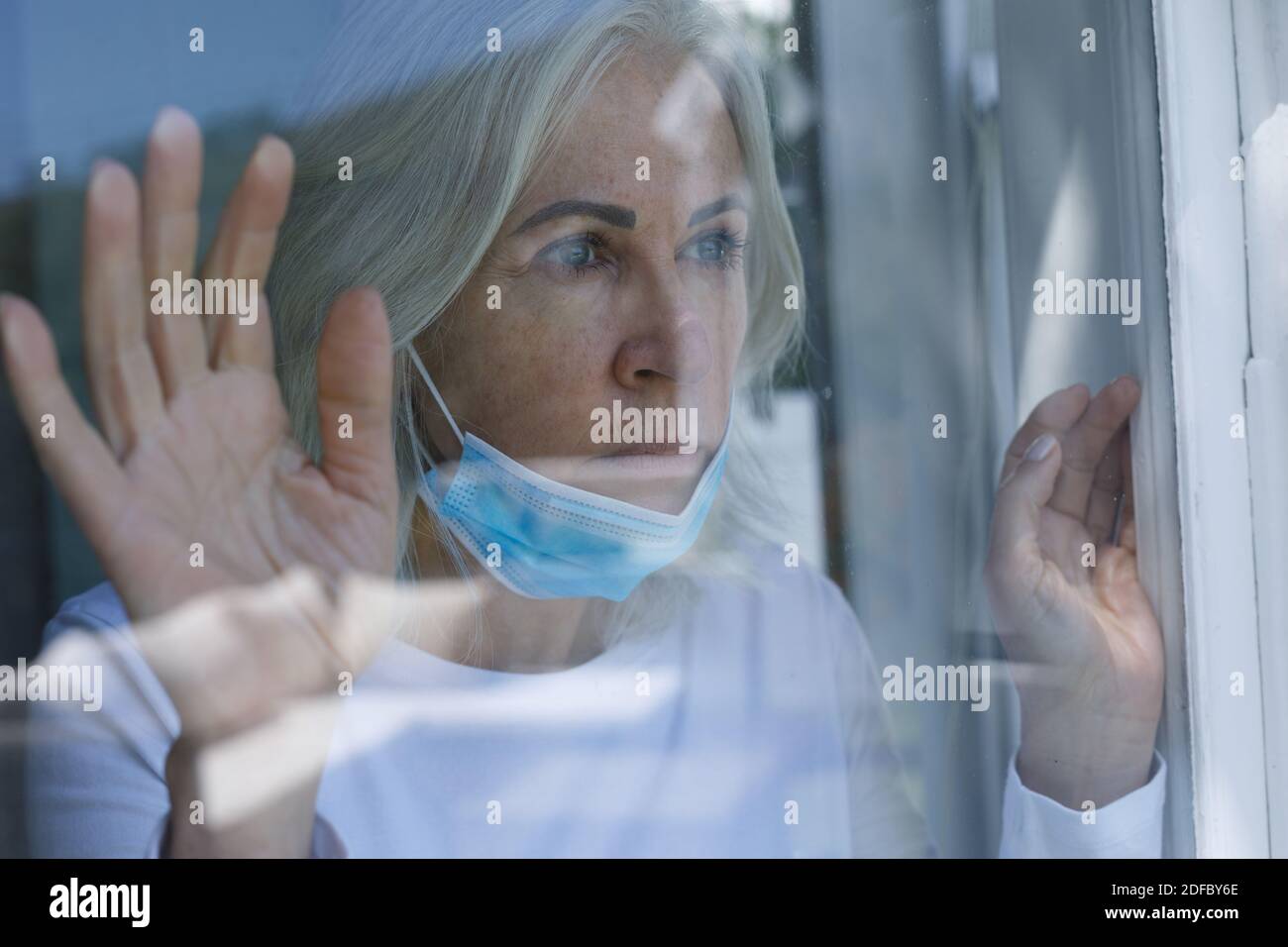 Femme caucasienne âgée avec un masque facial autour de son cou fenêtre en verre à la maison Banque D'Images