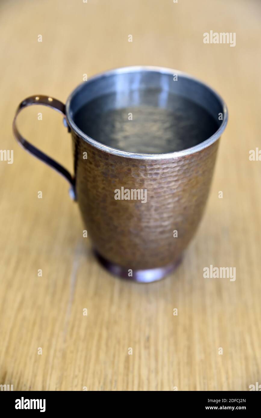 Un gros plan d'une tasse de cuivre remplie d'eau sur une surface en bois Banque D'Images