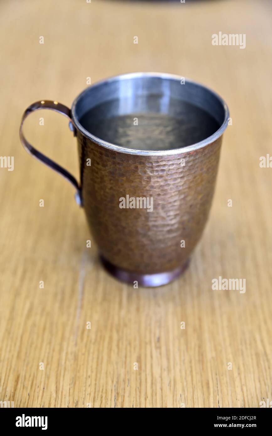 Un gros plan d'une tasse de cuivre remplie d'eau sur une surface en bois Banque D'Images