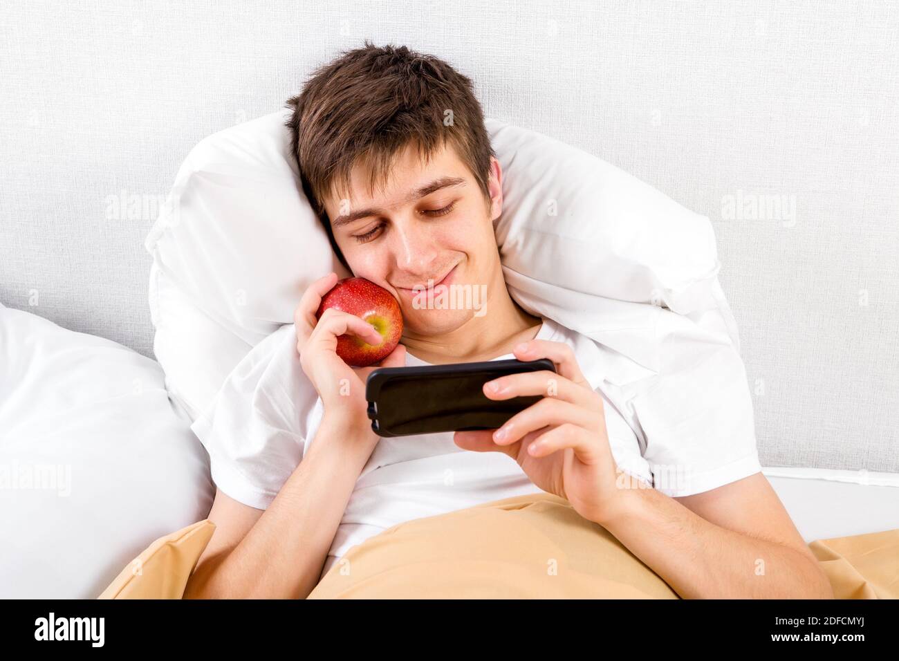 Jeune homme avec un Apple utilisez un téléphone dans le Lit à la maison Banque D'Images