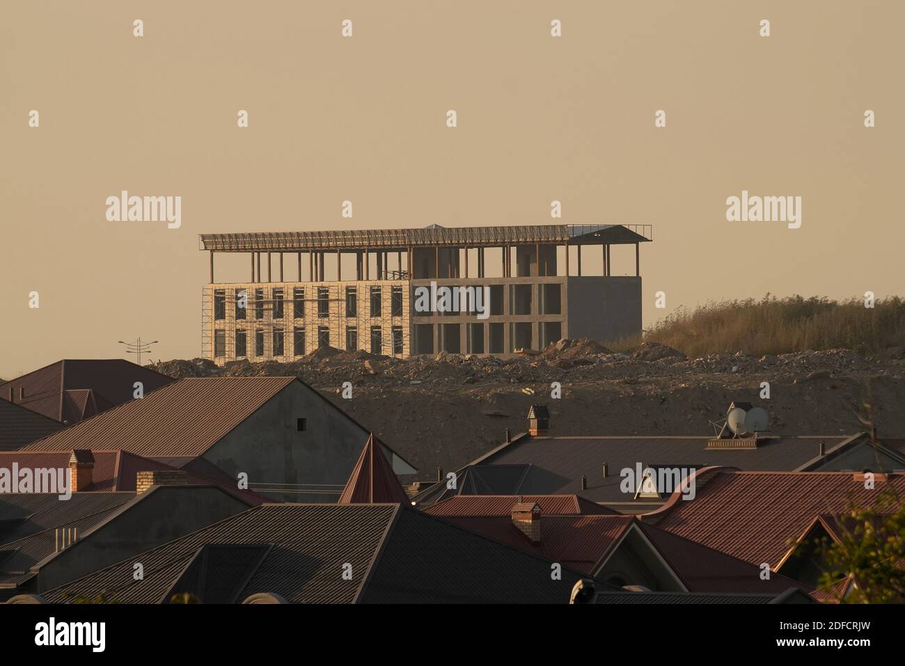 Un bâtiment solitaire inachevé sur une colline parmi les maisons à coucher de soleil Banque D'Images