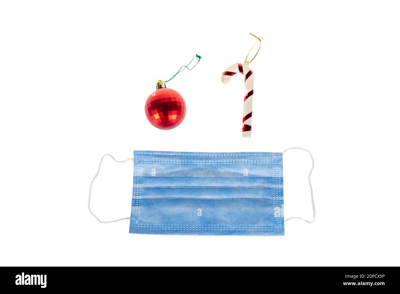 Décoration de Noël sur fond blanc de canne à sucre, boule rouge de noël et masque médical de protection pour Covid-19. Isolé sur blanc. Banque D'Images