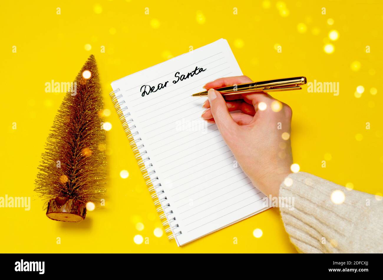 Femme écrivant à la main la lettre au Père Noël sur fond jaune et les lumières de bokeh. Arbre de Noël doré et cher Santa écriture. Concept de Noël. Banque D'Images