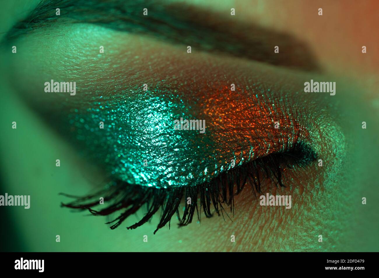 Gros plan extrême de l'iris oculaire femelle sous la lumière du néon. Femme avec beau maquillage, ombres à paillettes et faux cils. Yeux verts pour filles. Vie nocturne, nuit Banque D'Images