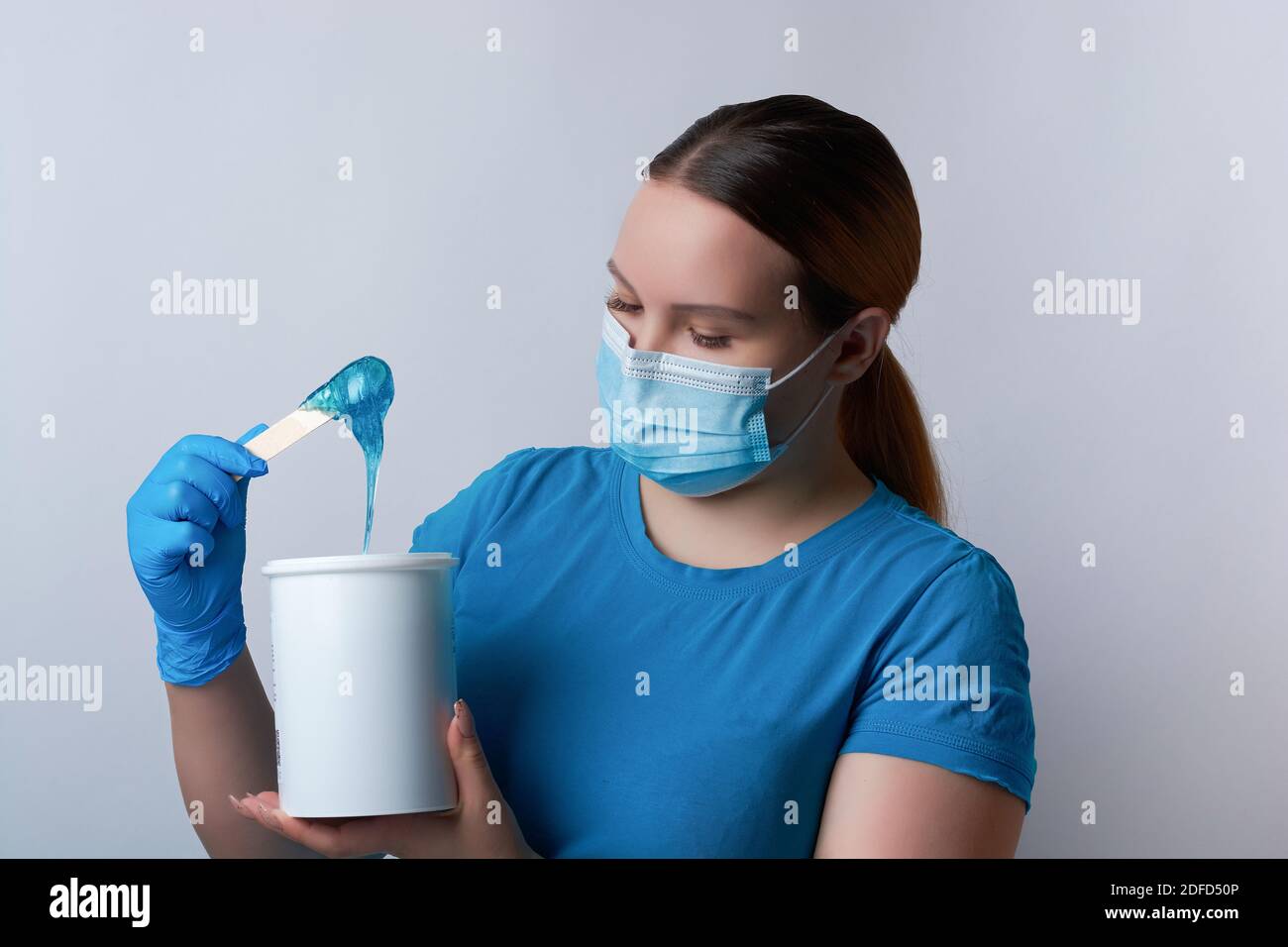 Un maître sugaring en gants bleus et un masque médical tient un bâton de cire de sucre bleu. Épilation et concept de beauté Banque D'Images