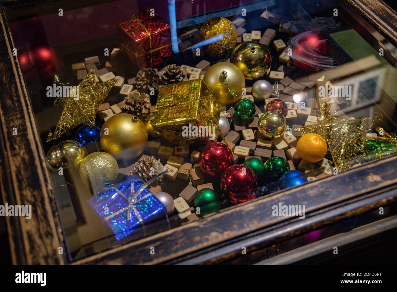 Table basse vintage avec boules de Noël colorées, brocart emballage cadeaux de Noël et cubes de bois de mahjong sous plan d'examen en verre avec des reflets flous. Tr Banque D'Images