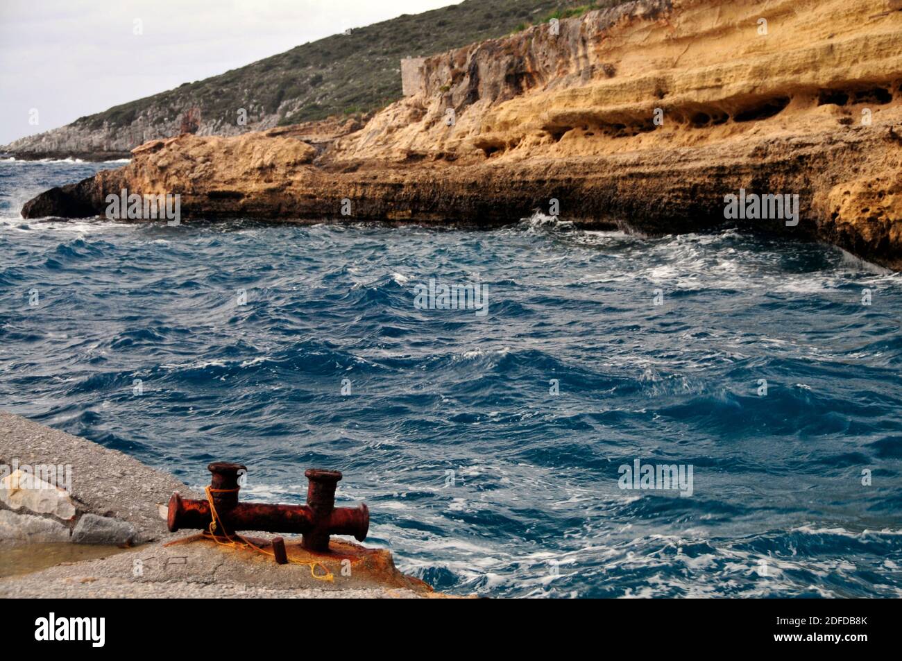 Bollard rouillé sur un quai au bord de la mer, avec rive rocheuse à travers l'entrée, mani, Grèce Banque D'Images