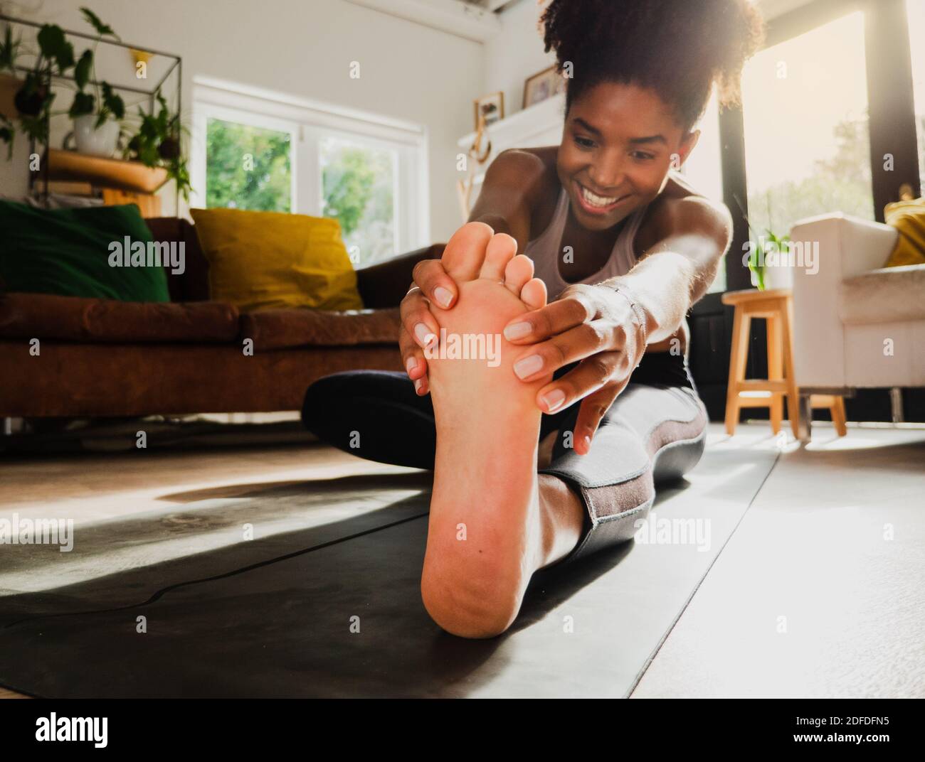 Belle femme motivée qui stretse les chaînes après une séance de yoga intense, assise sur un tapis de yoga gris dans le salon spacieux. Banque D'Images