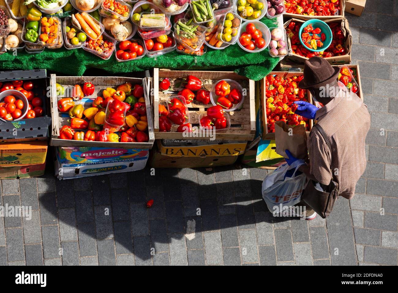 Vue d'en haut d'un homme inspectant des légumes dans un arrêt de rue à Brixton Market, Electric Avenue, Brixton, Londres Banque D'Images