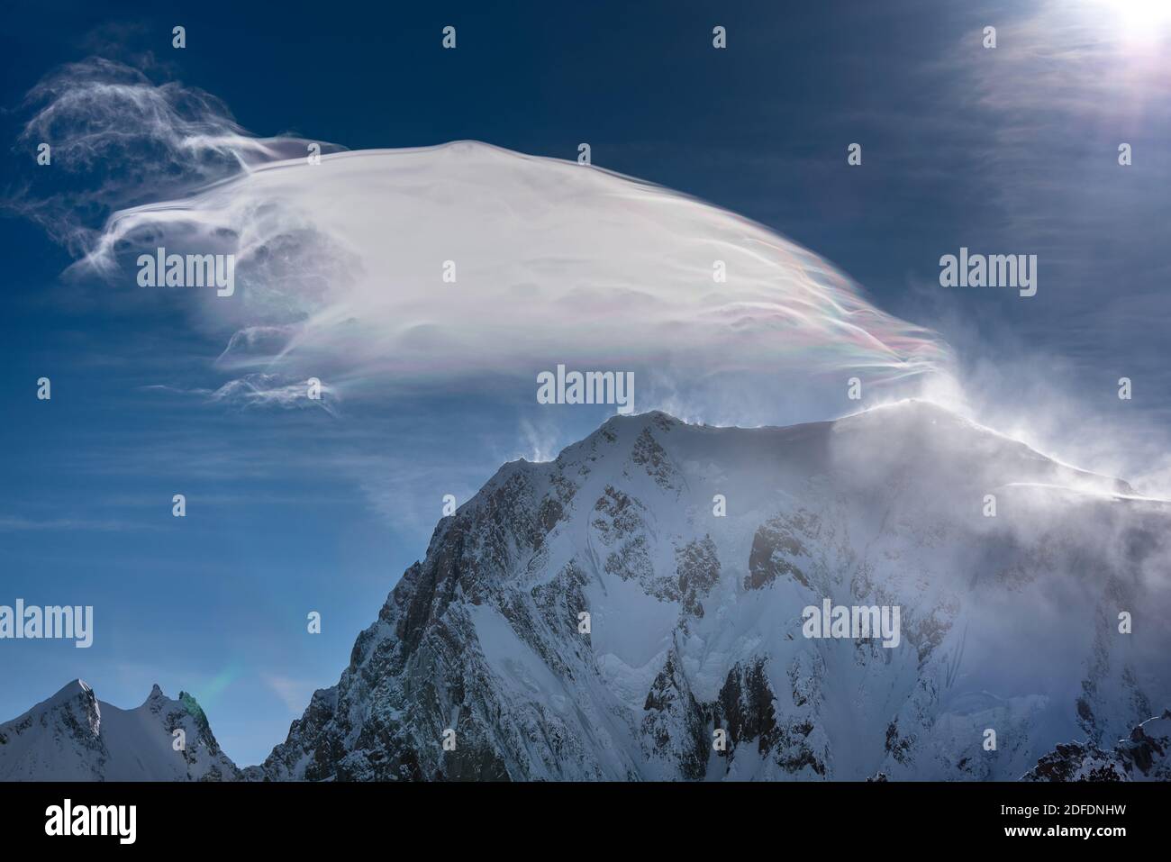 Un vent fort souffle la neige sur un sommet de montagne créant un étrange nuage irisé dans la lumière du soleil contre un ciel bleu profond Banque D'Images