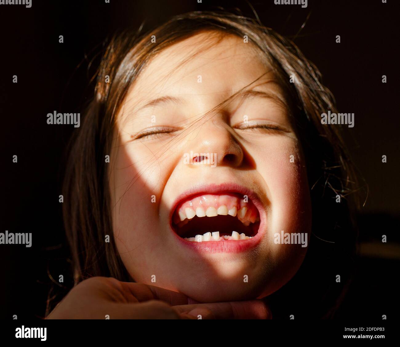 Une petite fille avec les yeux fermés inclinant la tête vers le haut afficher la première dent perdue Banque D'Images